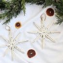 two white clothespin snowflakes on a white background with dried orange slices and a green garland