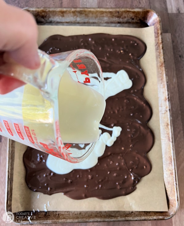 Pouring white chocolate over the melted chocolate for candy bark.
