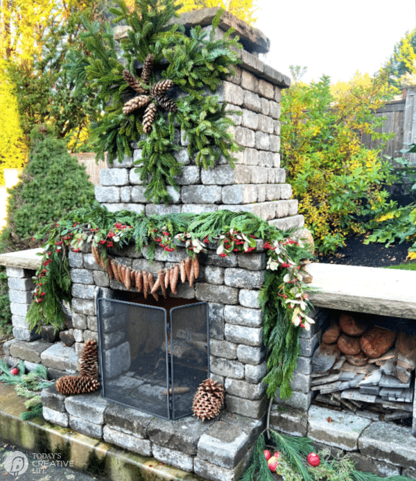 outdoor holiday decorating ideas for Christmas. Outdoor fireplace with pinecone and cedar garland. 