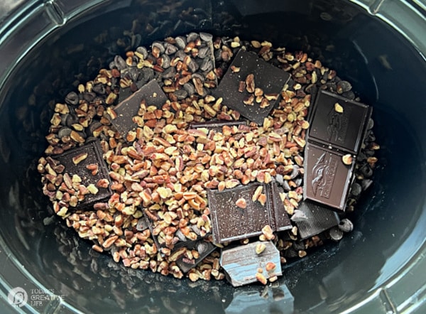 Chocolate squares and pecans in a dark crock pot. 