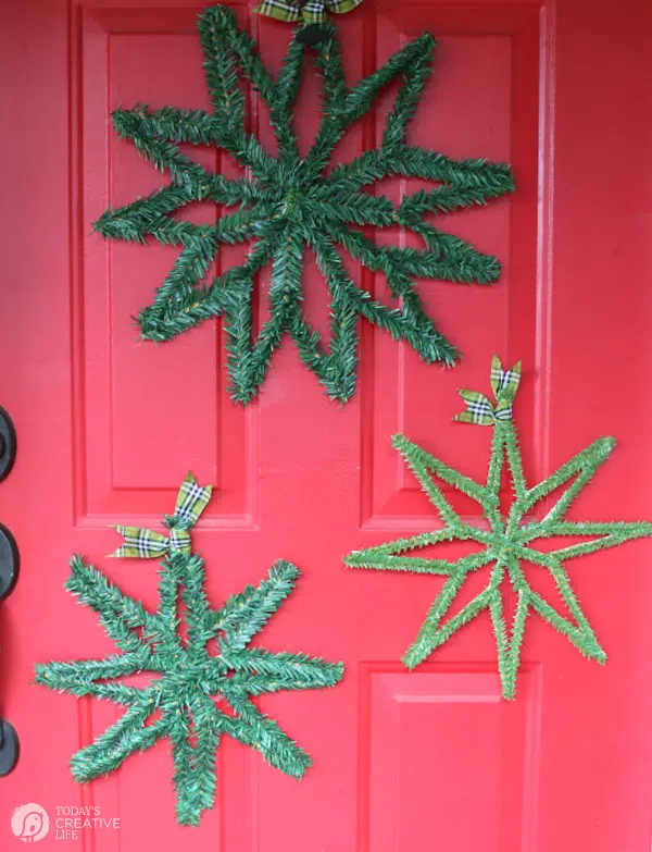three green evergreen stars hung on red door.