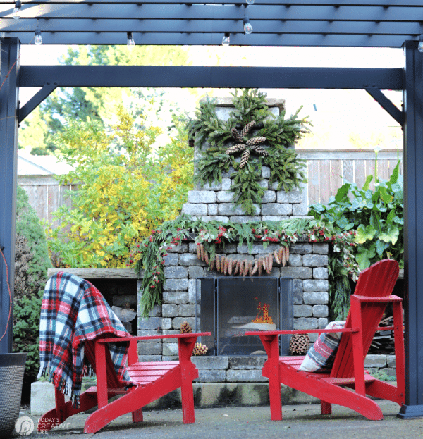 Outdoor holiday decorating ideas for Christmas - outdoor fireplace with red Adirondack chairs. 