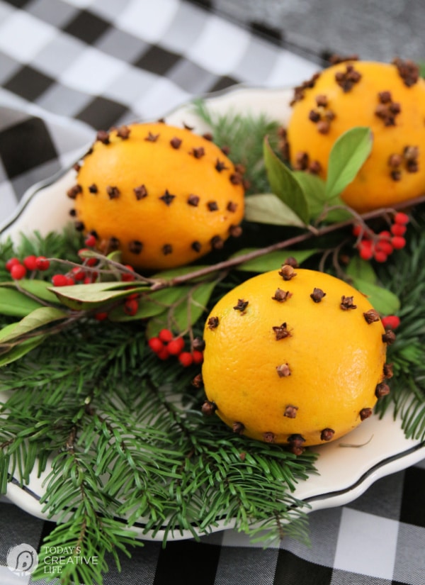 Three Orange Pomanders in a dish with pine greens and red berries