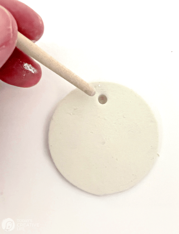 Poking a hole in a piece of round white clay for making Christmas ornaments DIY
