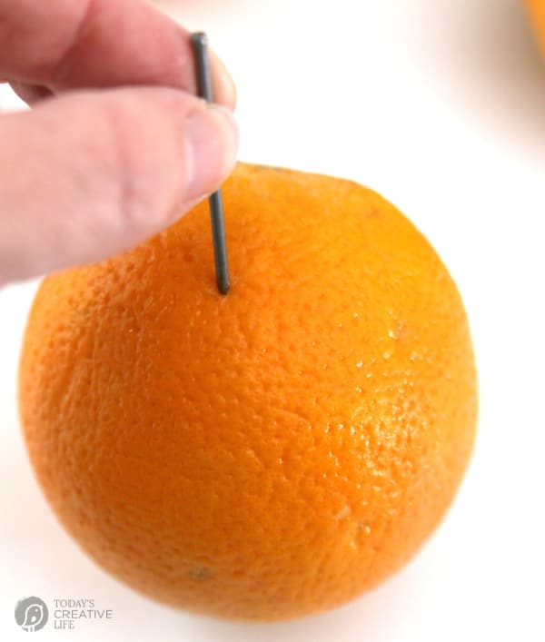 poking a nail into an orange for making orange clove pomanders.