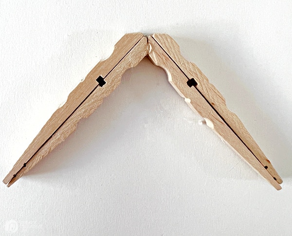 two wood clothes pins that have been glued together for making a snowflake.