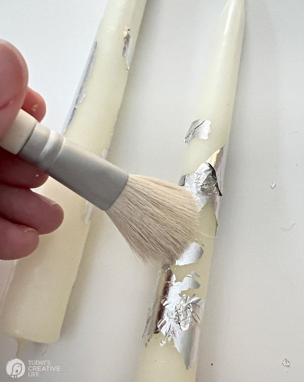 Using a brush to brush off excess gold leaf on candle | DIY Gold Leaf Candle craft
